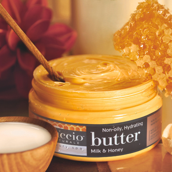 Jar of milk and honey butter with a wooden spoon and honeycomb on a wooden surface.