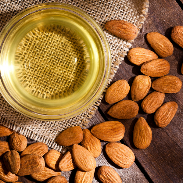 Almonds and a glass container of almond oil on a wooden surface