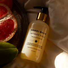 Bondi Wash intimate wash bottle with a plate of sliced fruit in the background