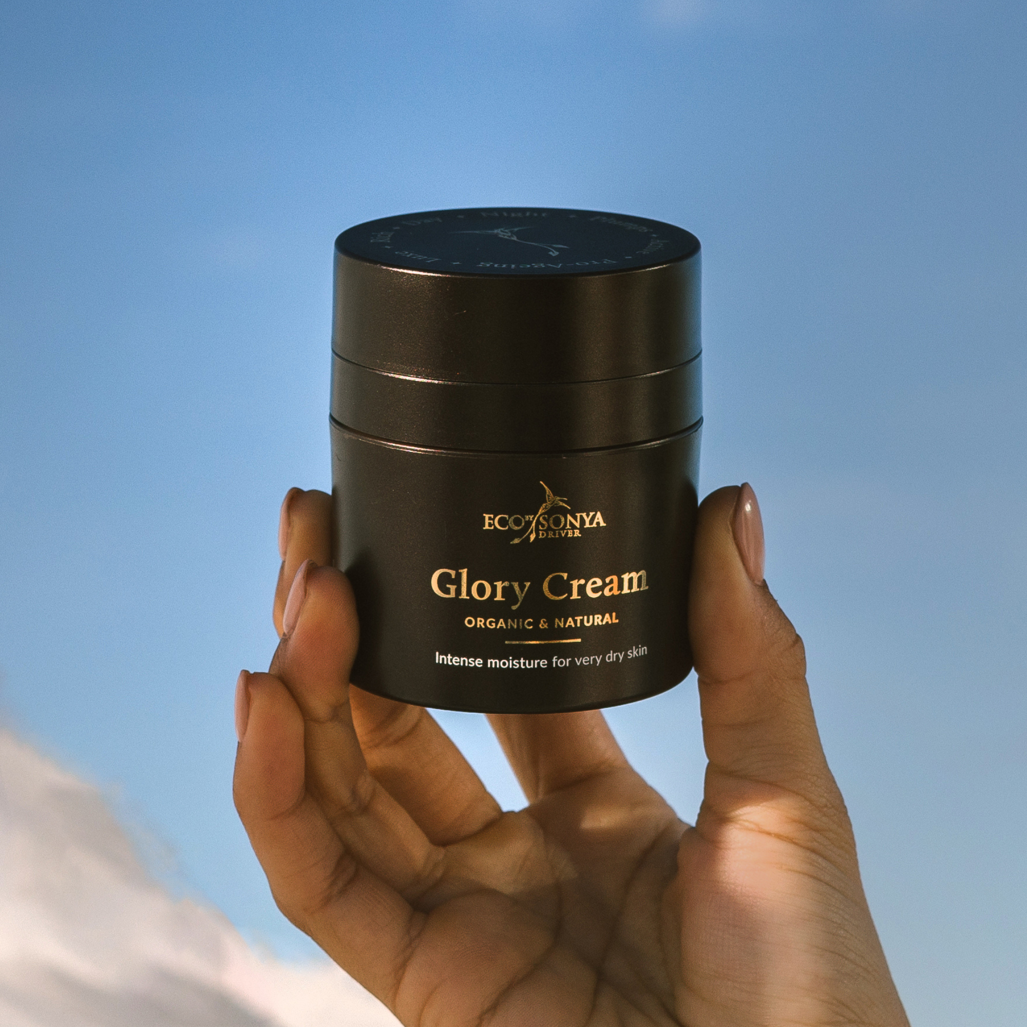 Hand holding a jar of Eco by Sonya Glory Cream against a clear blue sky
