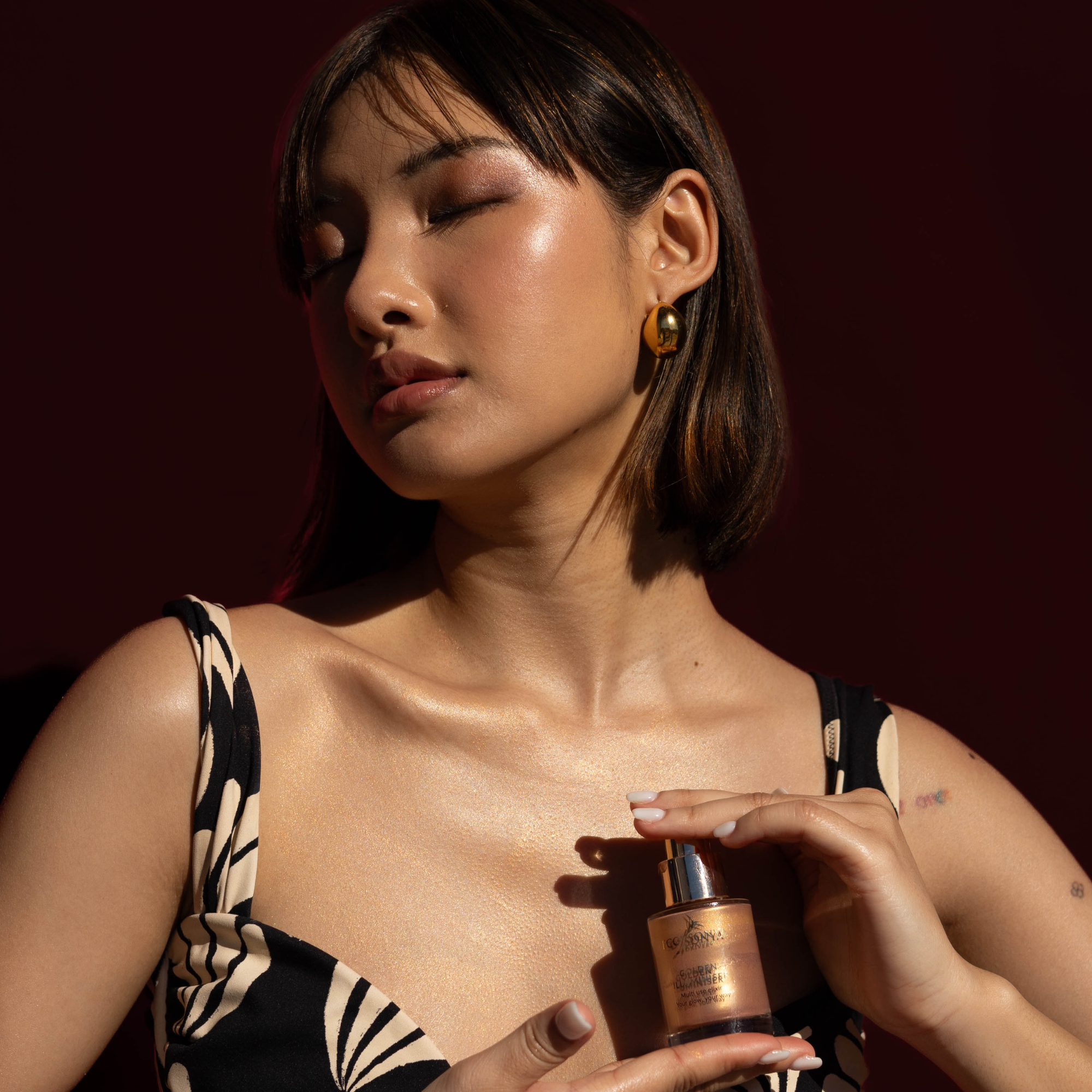 Woman holding Eco by Sonya Golden Illuminiser bottle against a dark background