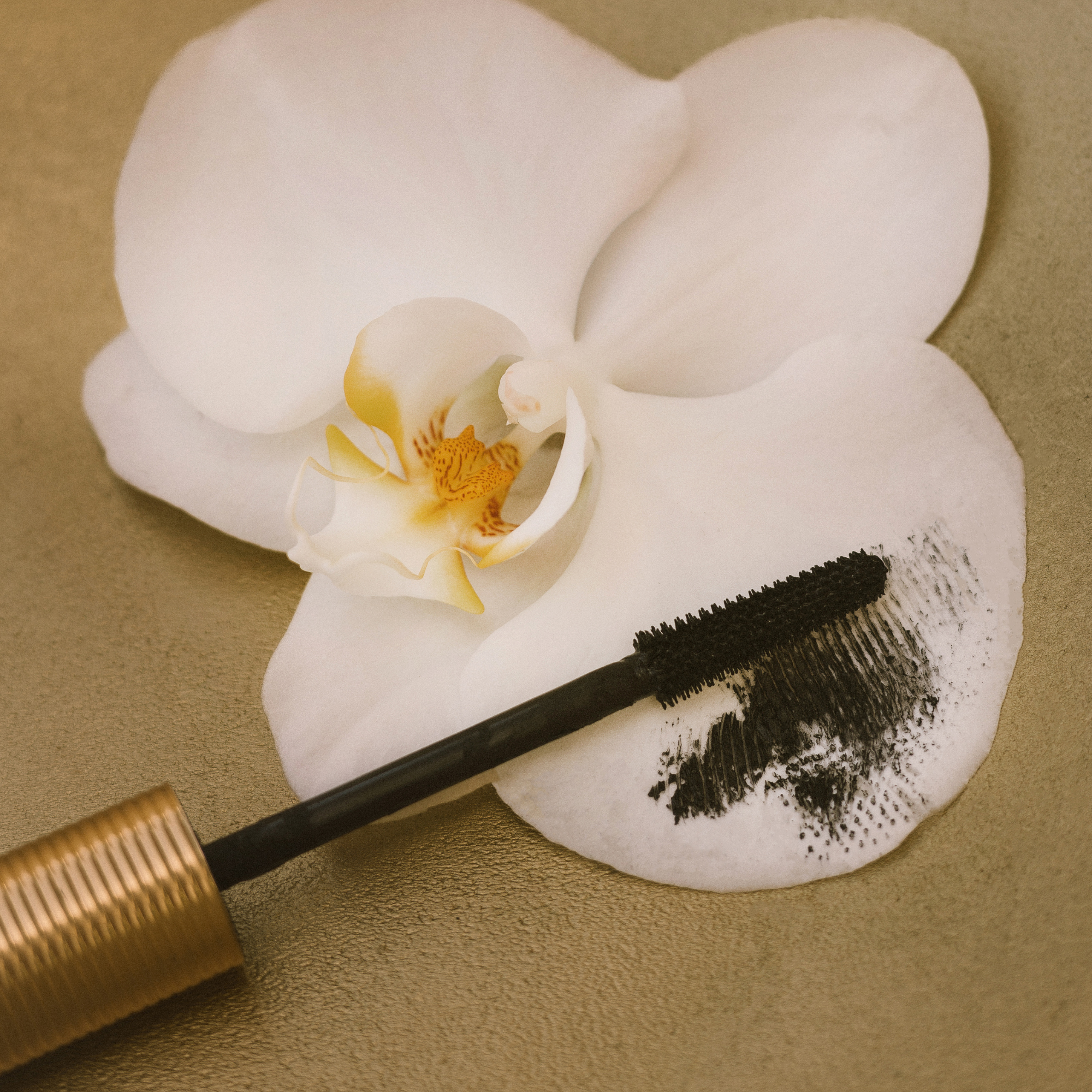 Eco by Sonya Driver Mitzi Mascara wand on a white orchid flower against a beige background