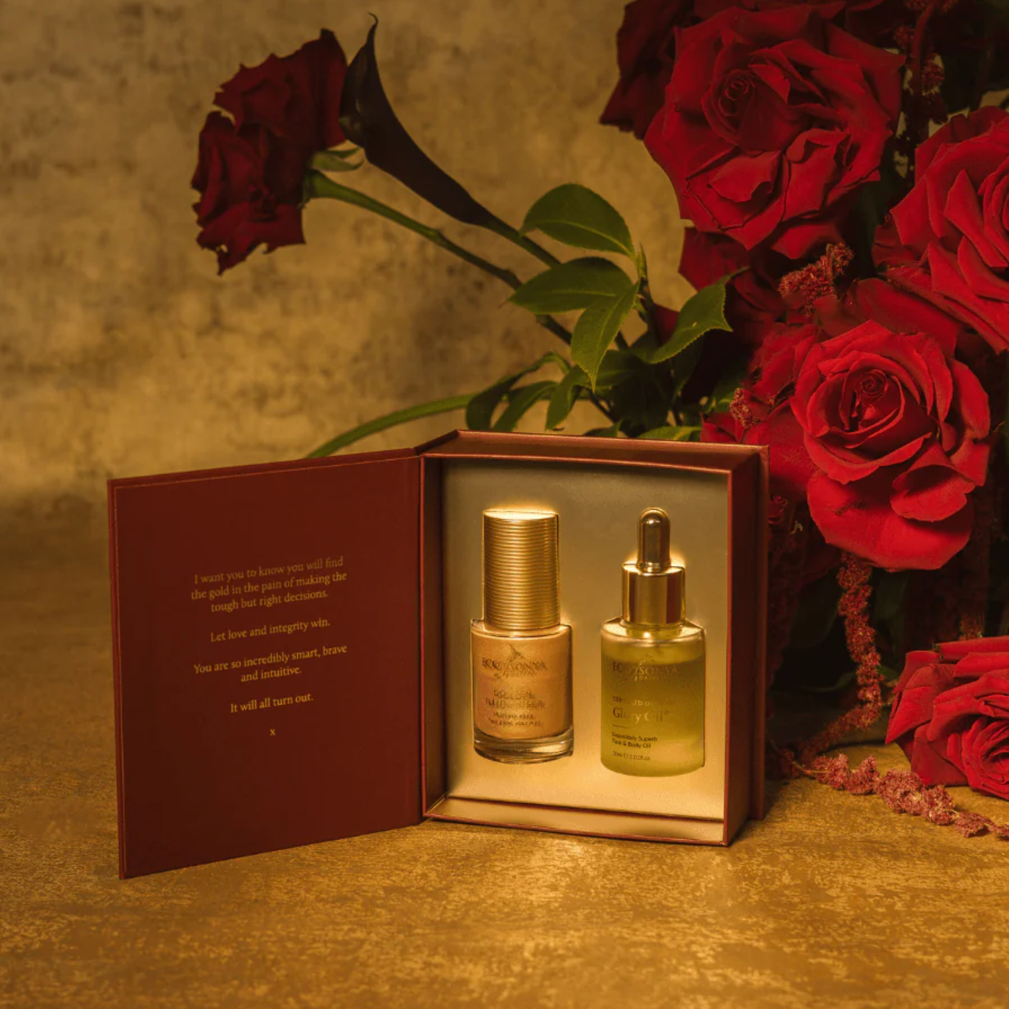 Two small bottles in an open box with a bouquet of red roses on a textured surface.