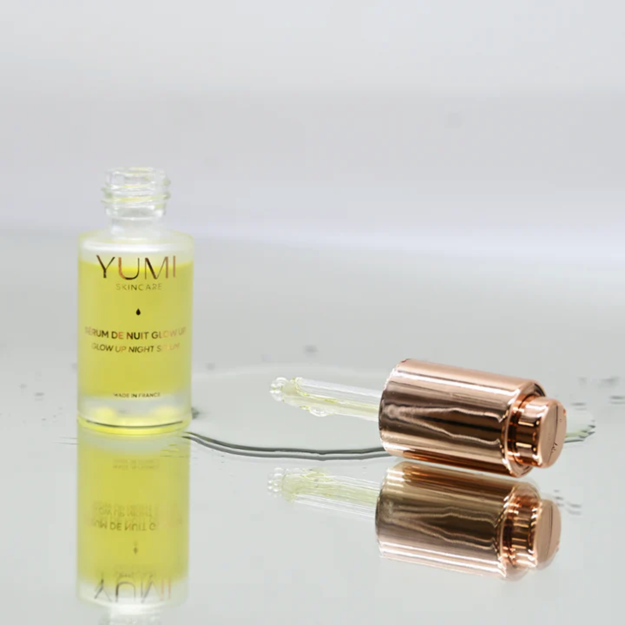 YUMI skincare serum bottle with rose gold cap on a reflective surface